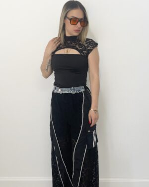 Donna indossa pantalone nero con gamba in pizzo, tasche cargo laterali, dettagli in denim e fondo regolabile.