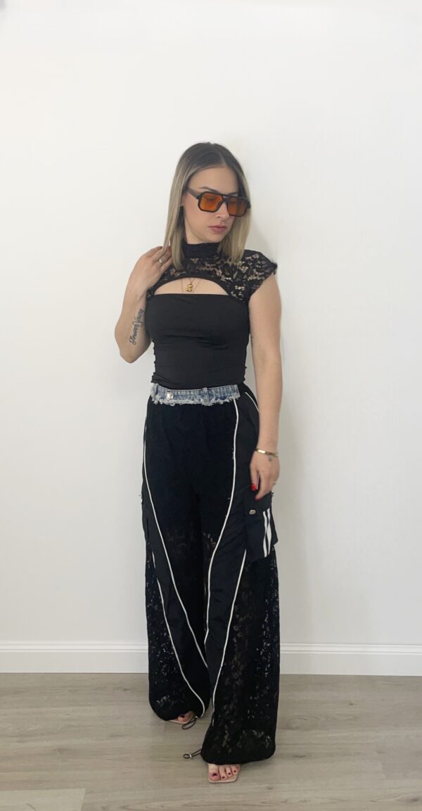 Donna indossa pantalone nero con gamba in pizzo, tasche cargo laterali, dettagli in denim e fondo regolabile.