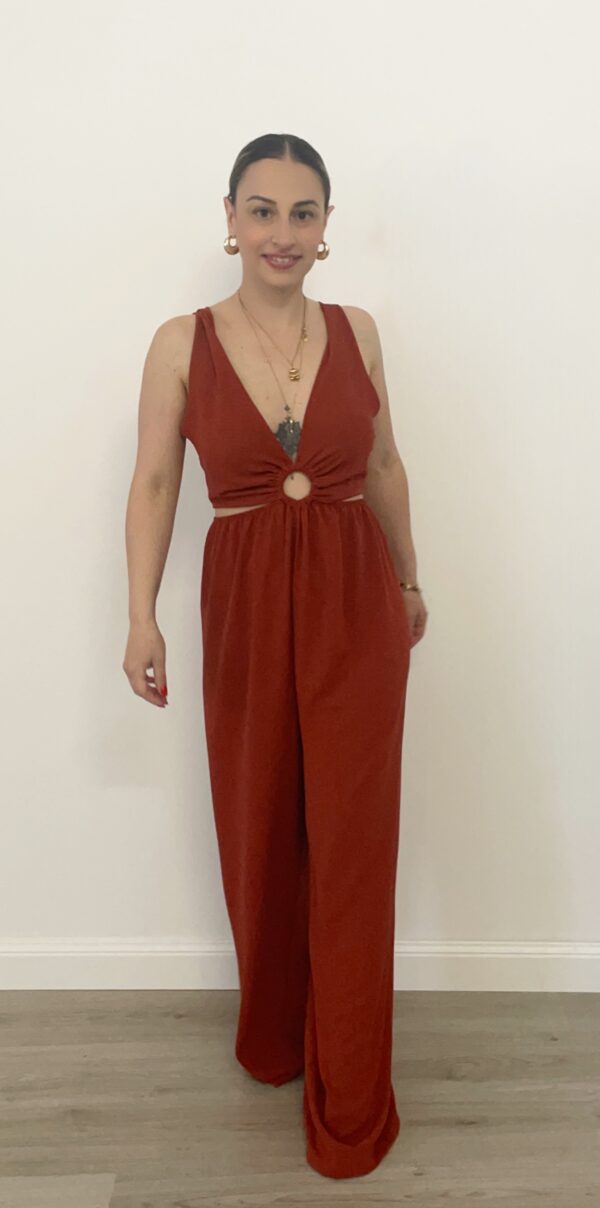 Jumpsuit in tessuto fluido color coccio, con scollo a V e cut-out rotondo al centro. I fianchi sono aperti con fascia elasticizzata che si adatta alle forme. Gamba palazzo ampia e laccetto regolabile dietro la schiena. Modello comodo, femminile e adatto fino alla taglia 48. La modella è alta 1,60 m e indossa la taglia S.