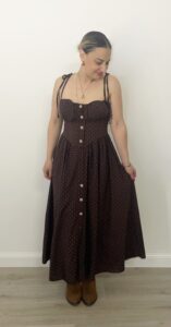 Abito midi marrone con micro pois bianchi, bottoni frontali, bustino sagomato e spalline da annodare. Indossato da modella alta 1,60 m, taglia S