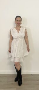 Abito corto bianco con pois neri, scollo incrociato, spalline da annodare e balza sul fondo. Indossato da modella alta 1,60 m, taglia S, con stivali texani neri.
