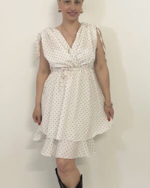 Abito corto bianco con pois neri, scollo incrociato, spalline da annodare e balza sul fondo. Indossato da modella alta 1,60 m, taglia S, con stivali texani neri.