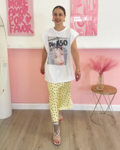 Donna indossa T-shirt bianca oversize con stampa tipo giornale, spalline strutturate e pantalone giallo a fiori.