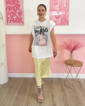 Donna indossa T-shirt bianca oversize con stampa tipo giornale, spalline strutturate e pantalone giallo a fiori.