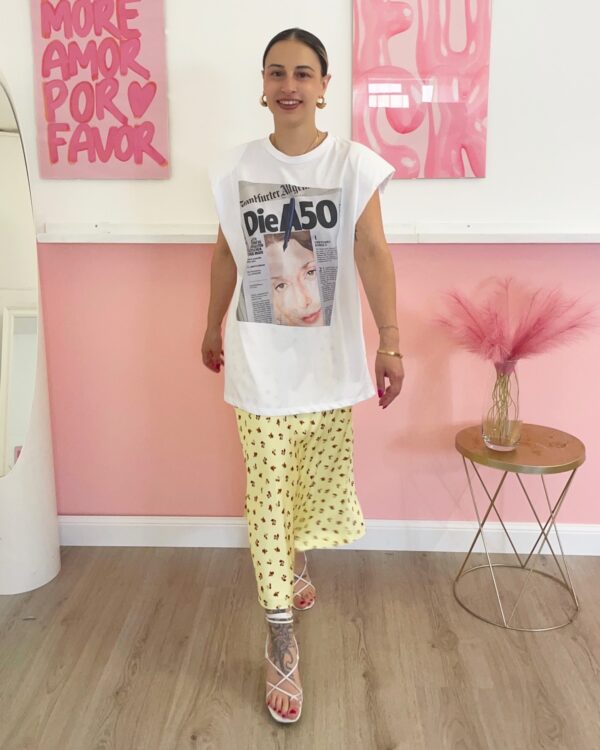 Donna indossa T-shirt bianca oversize con stampa tipo giornale, spalline strutturate e pantalone giallo a fiori.