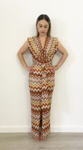 Donna indossa abito lungo con fantasia zigzag multicolor, scollo a V e nodo in vita