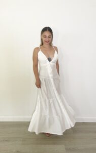 Abito lungo bianco con spalline sottili, scollo a V profondo con coppe, bottoni veri frontali e balze leggere.