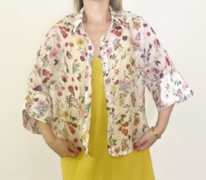 Camicia leggera a fantasia floreale con maniche ampie tre quarti, indossata aperta o annodata sul davanti.
