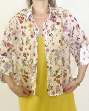 Camicia leggera a fantasia floreale con maniche ampie tre quarti, indossata aperta o annodata sul davanti.