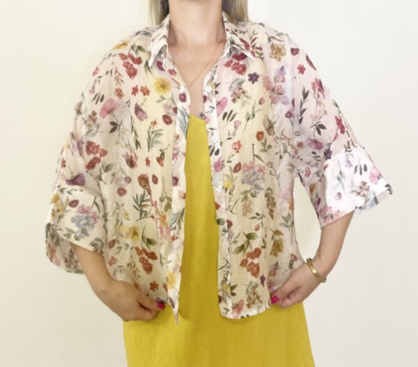 Camicia leggera a fantasia floreale con maniche ampie tre quarti, indossata aperta o annodata sul davanti.