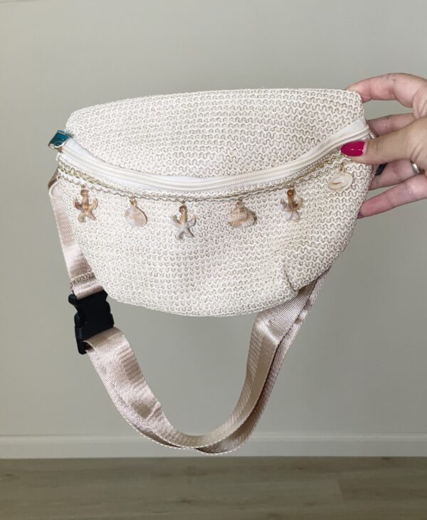 Marsupio in paglia intrecciata beige con ciondoli a tema marino e tracolla regolabile.
