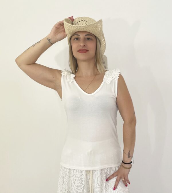 Canotta bianca senza maniche con scollo a V e rouche sulle spalle, indossata da modella con cappello di paglia.