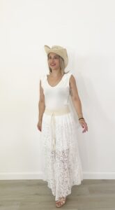 Pantaloni ampi in pizzo beige panna con elastico in vita e fodera interna, indossati con canotta bianca e cappello di paglia.
