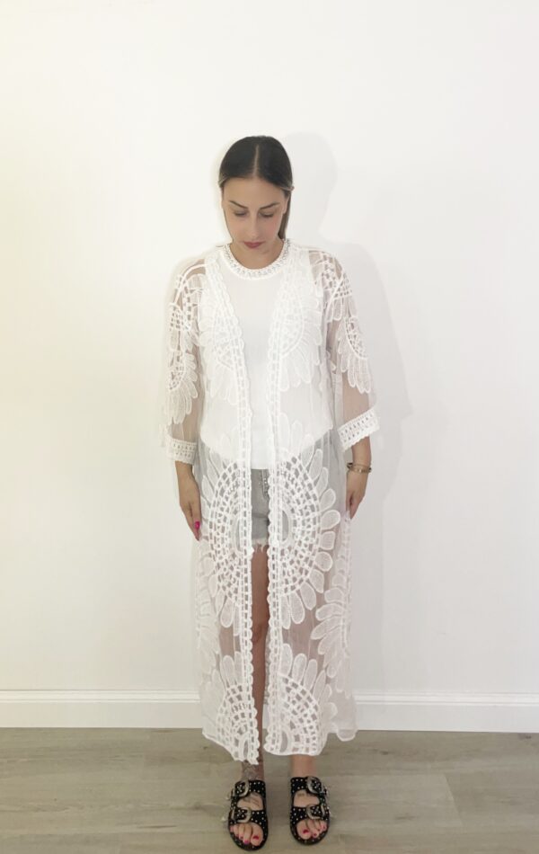 “Kimono lungo in pizzo bianco con motivo floreale indossato da modella su top bianco e shorts, vista frontale.”