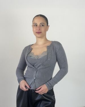 Cardigan grigio con bottoni e inserto frontale effetto canotta bordato in pizzo, indossato con pantaloni neri.