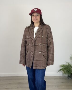 Giacca doppiopetto Principe di Galles marrone indossata con felpa bianca e jeans blu.
